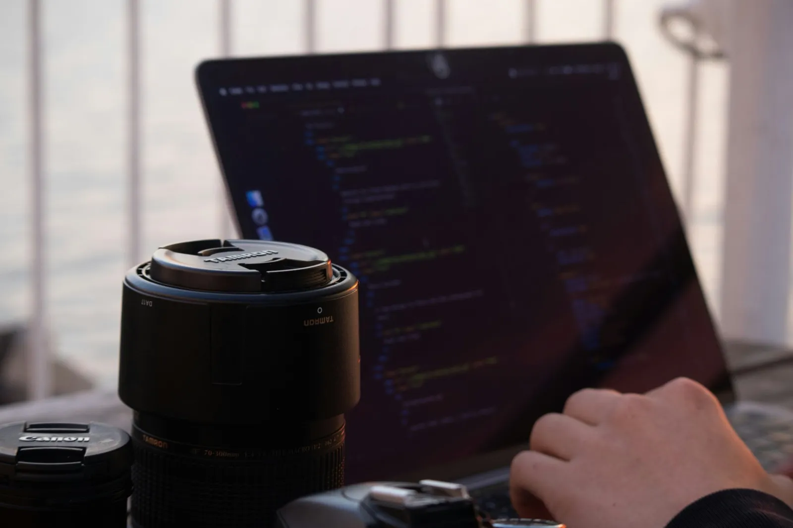 Camera lens on desk with laptop showing development environment